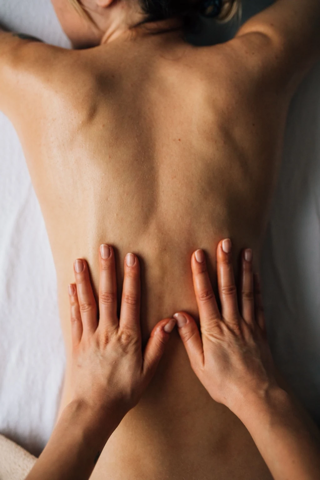 Hands applying remedial massage treatment to the lower back of a client lying face down